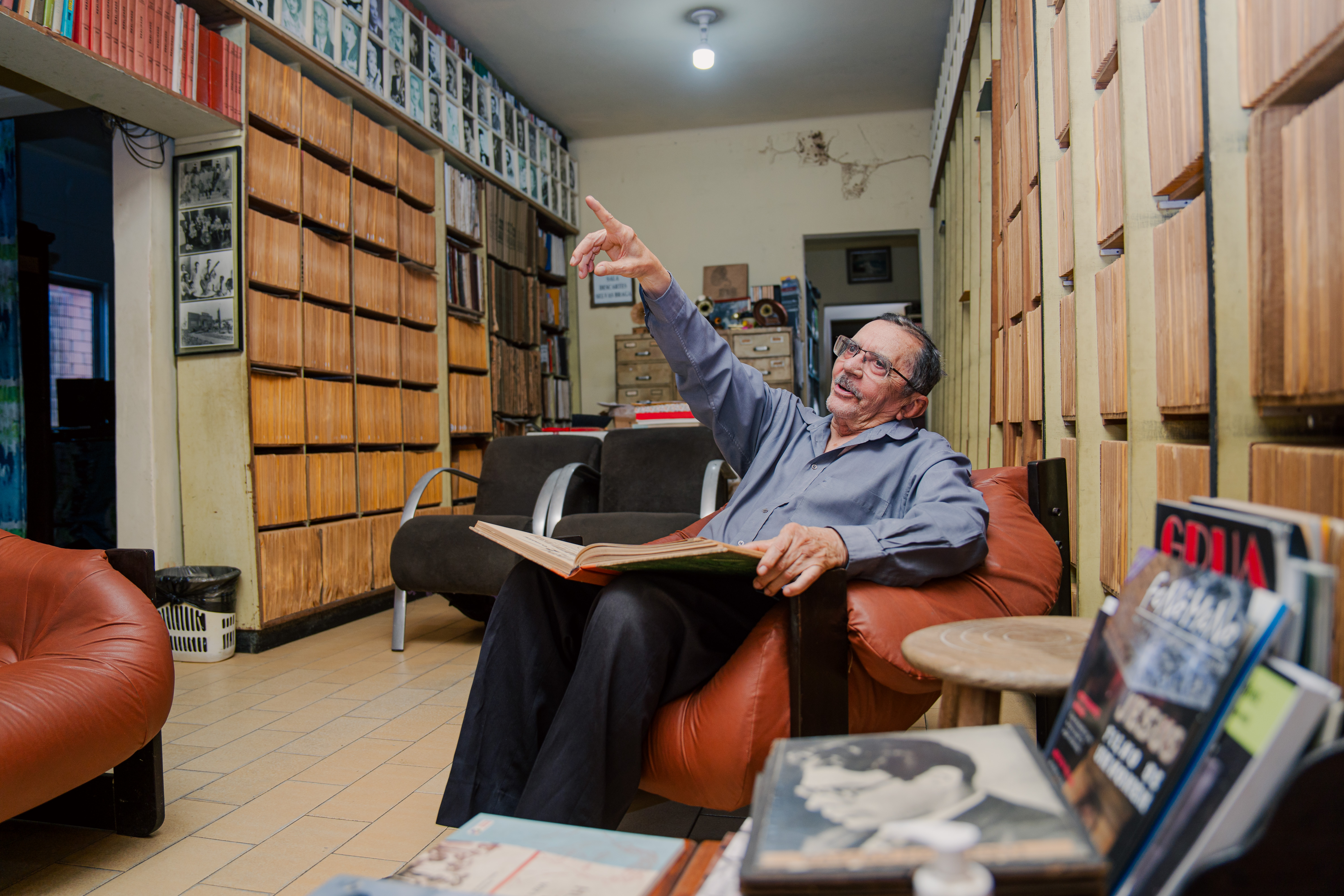 Nirez sentado em sua sala na frente de suas estantes de discos